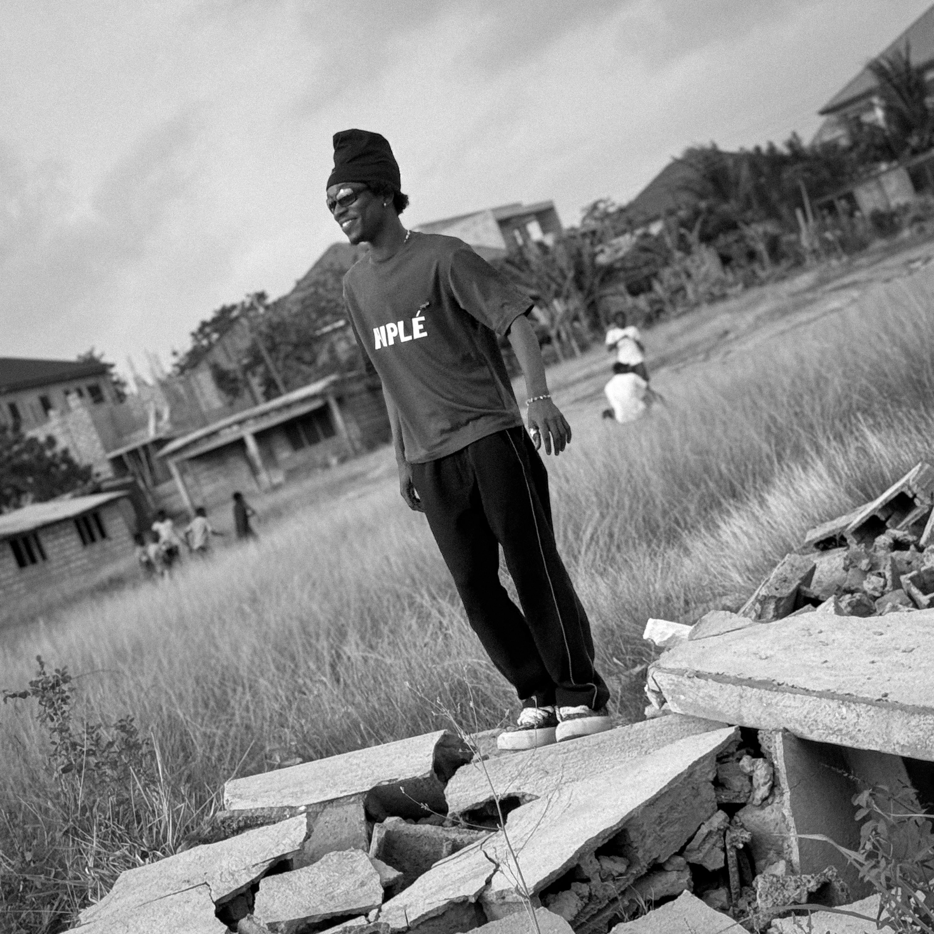 Person wearing a HIPLÉ shirt standing on rubble with a cloudy sky and buildings in the background. Location Ghana, West Africa