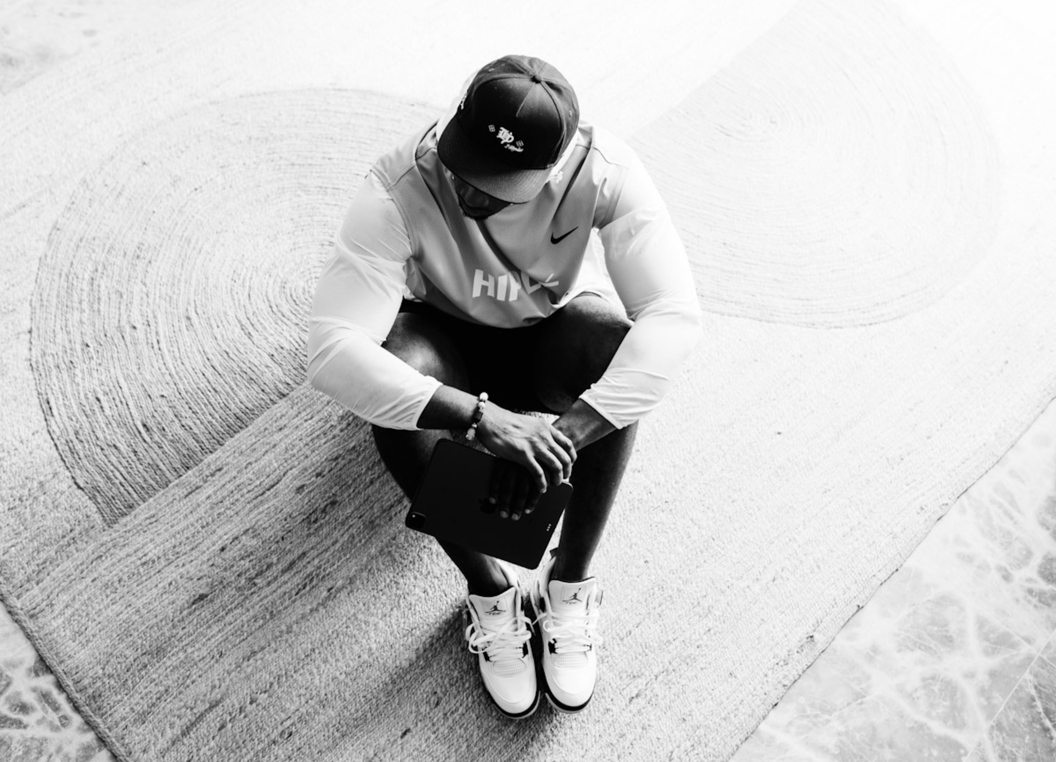 Person sitting on a textured pavement wearing a Nike cap and shoes.